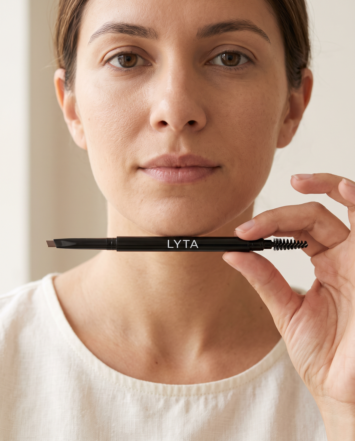 LYTA Automatic Eyebrow Pencil in Ash Brown, model holding the original double-ended pencil with angled tip and brush
