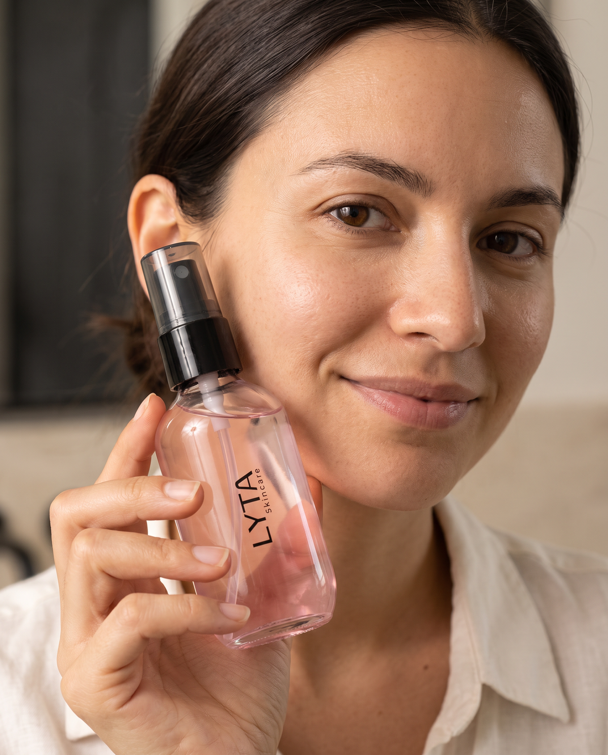 LYTA Oil Control Setting Spray, model holding the original pink bottle with a black pump and clear protective cap