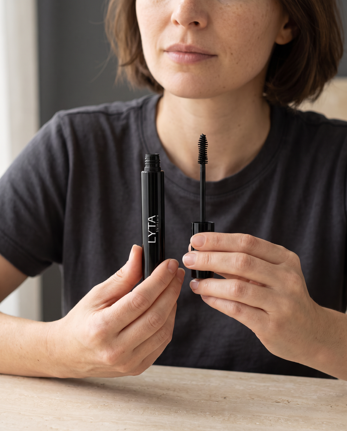 LYTA Mascara, hands holding the original black tube and separate mascara wand