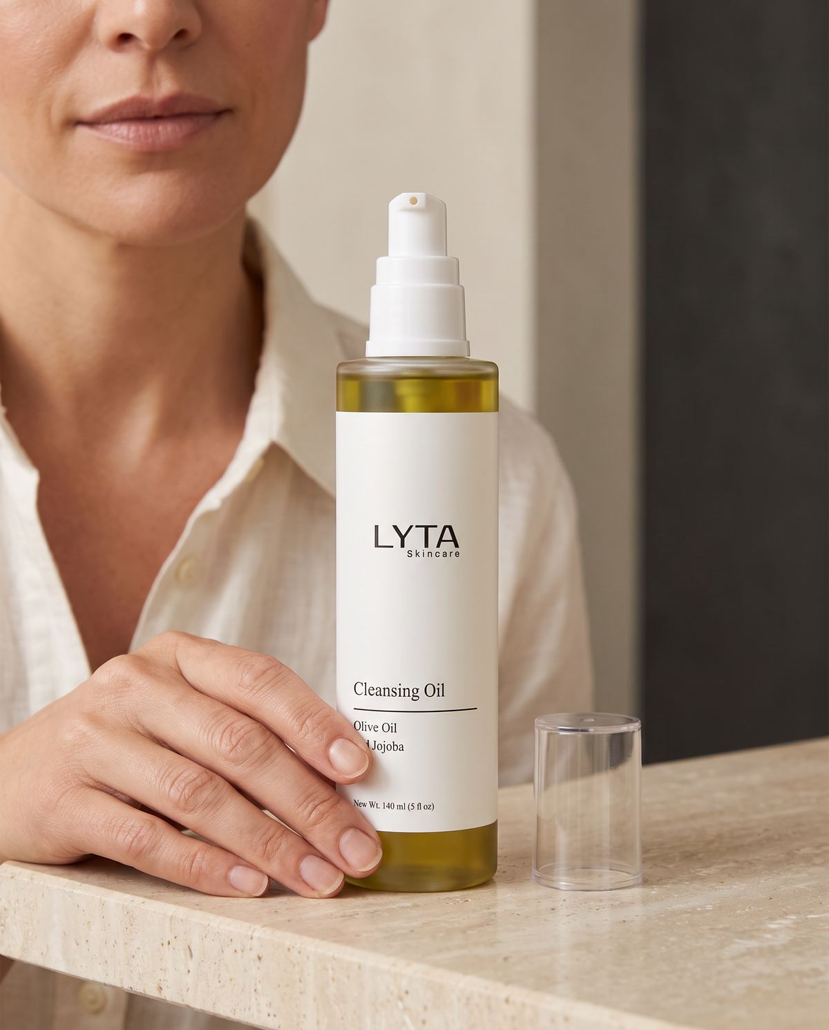 LYTA Cleansing Oil, original bottle and clear cap resting on a stone surface with a hand holding the bottle